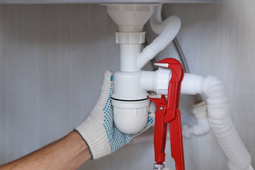 Technician in navy shirt installing plumbing under a sink in a kitchen cabinet