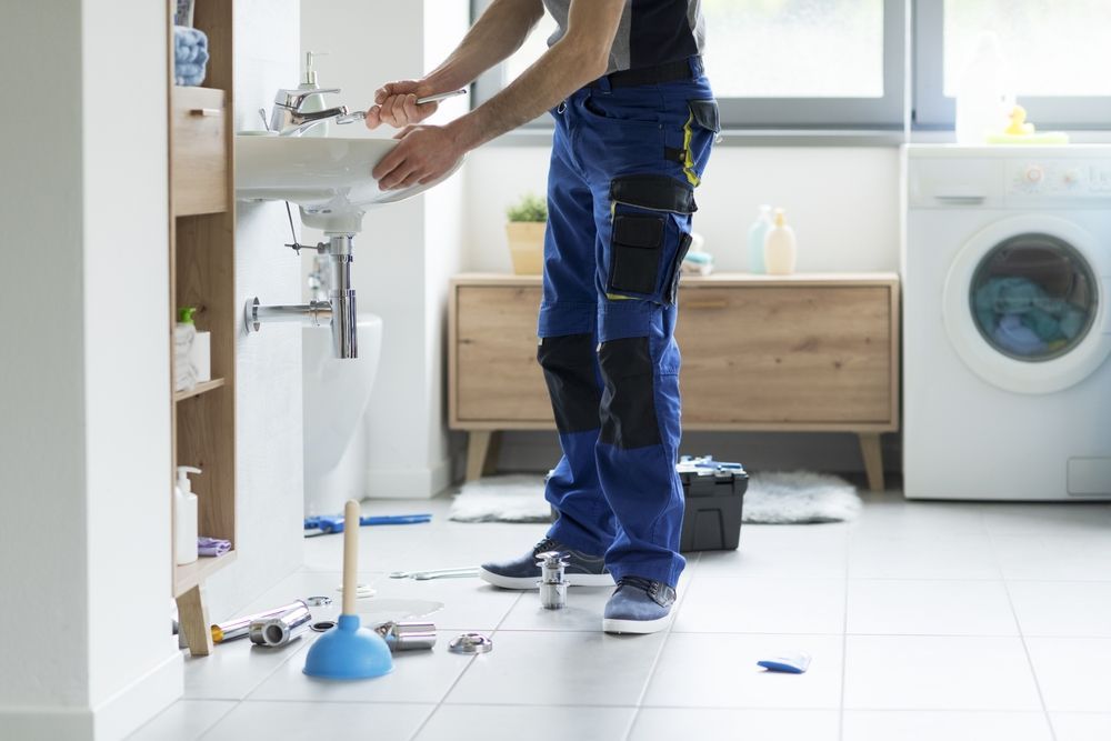 Person installing a sink in a bright laundry room, with tools on the floor and a washing machine nearby