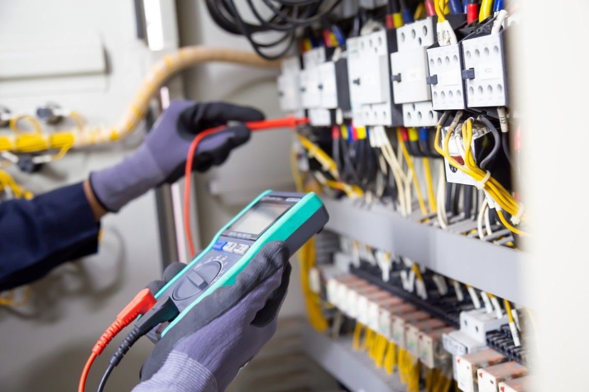 Technician testing electrical wiring with a multimeter in a control panel