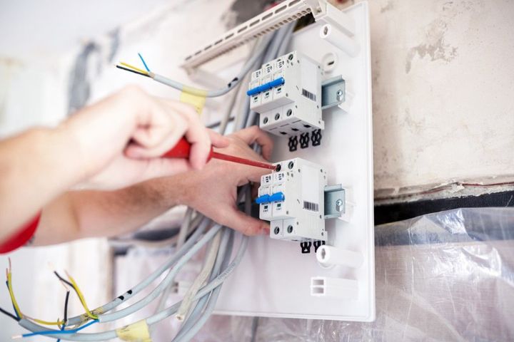 Hands wiring an electrical circuit breaker panel with red and yellow tools