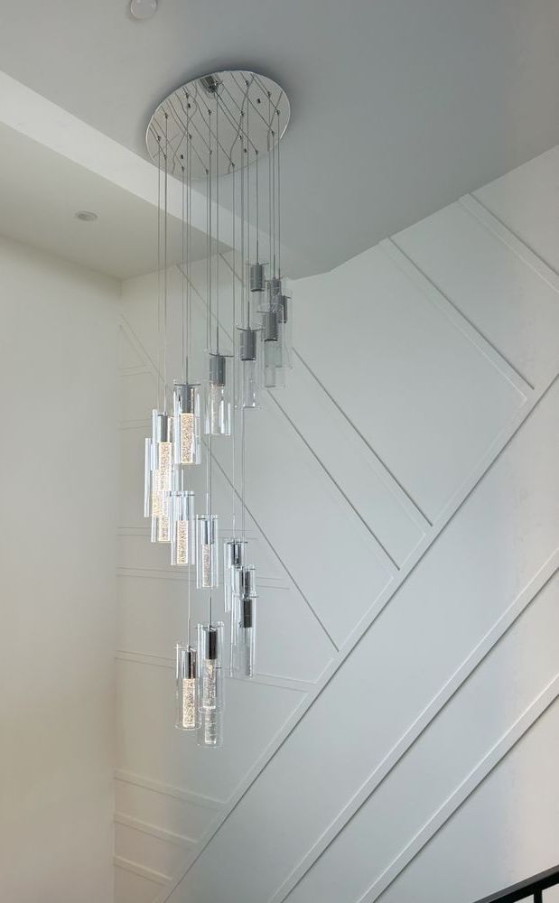 A long chandelier is hanging from the ceiling above a staircase.