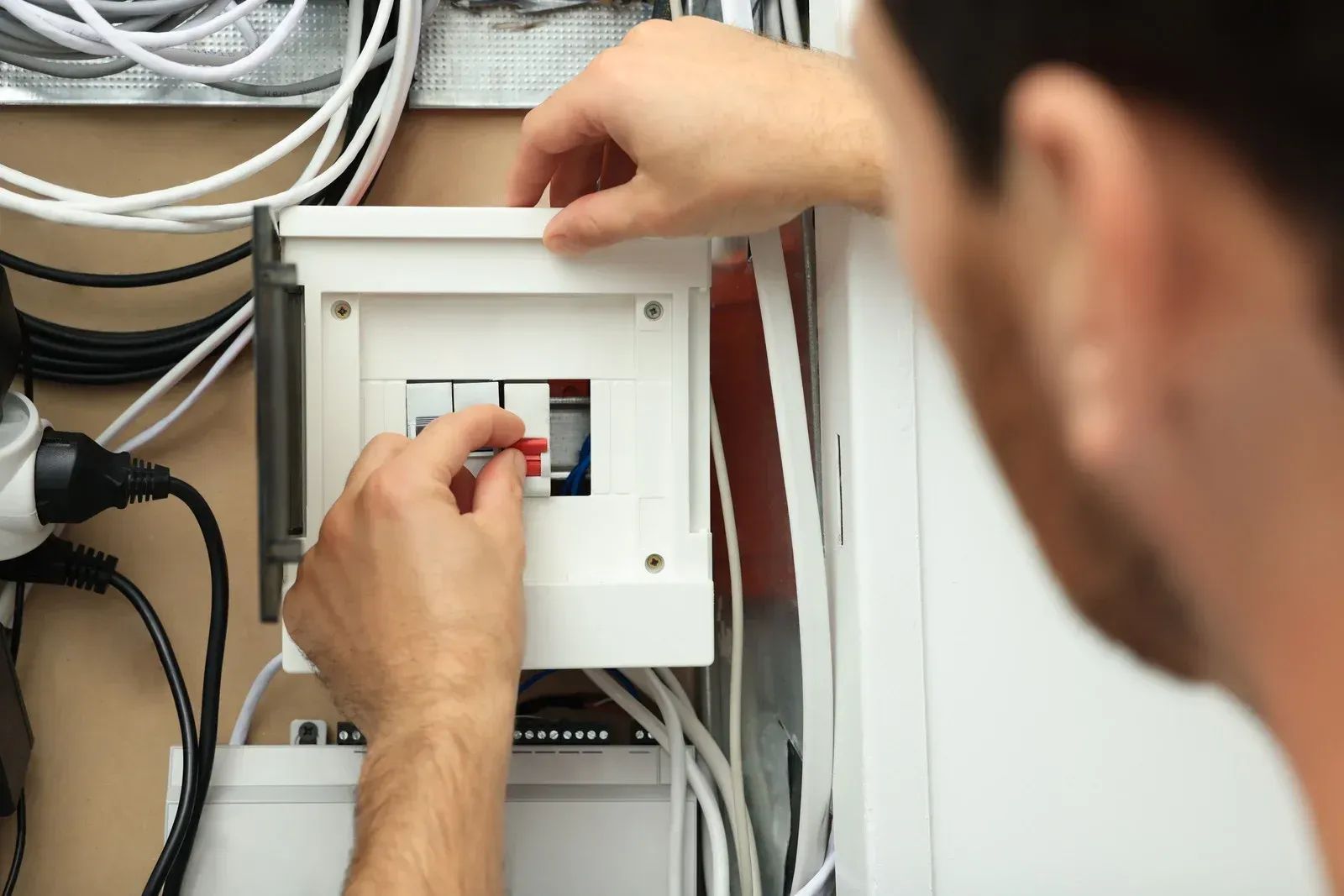 Technician adjusting wiring inside an electrical control panel with cables around it