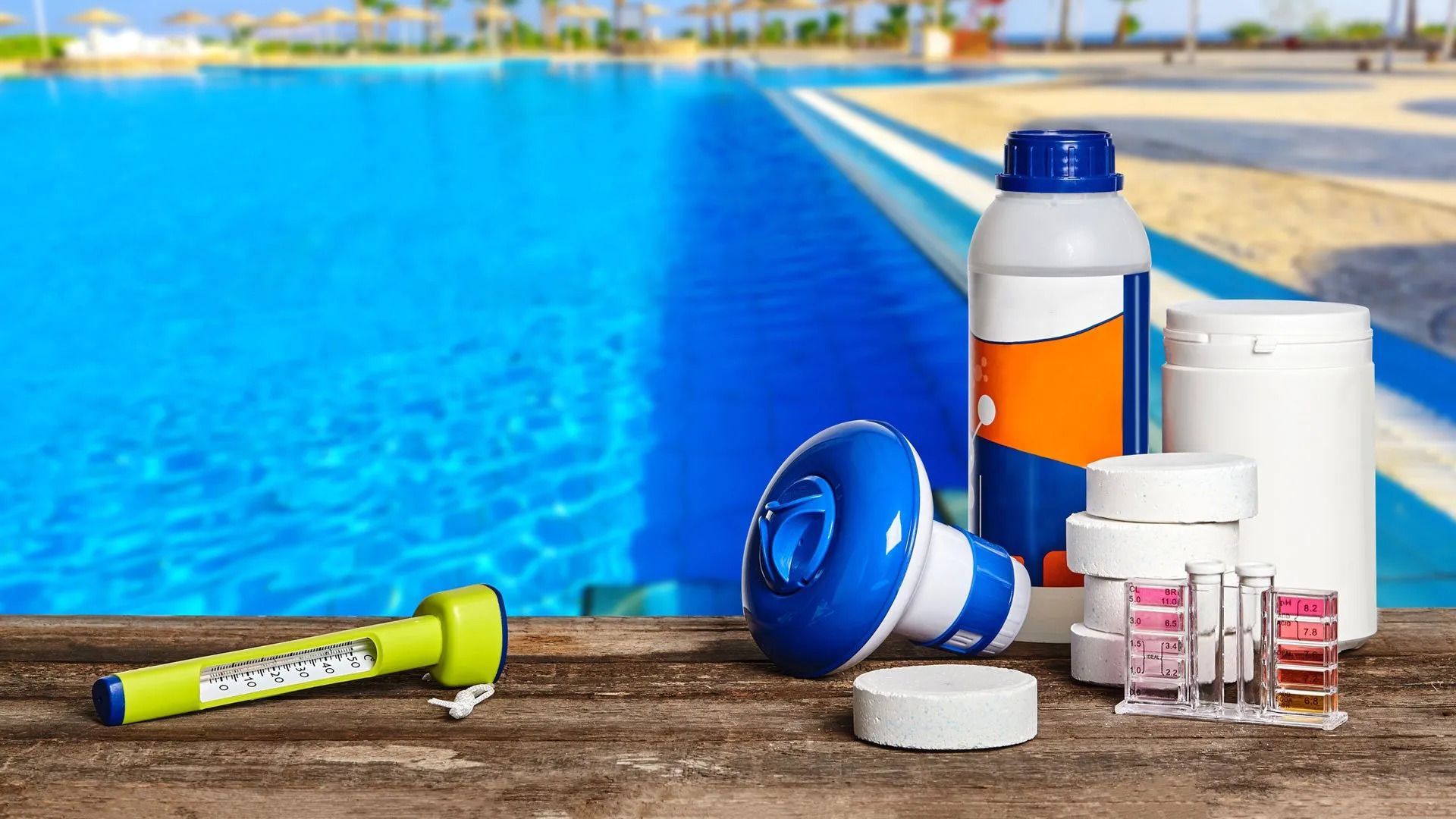 A bunch of chemicals on a wooden table next to a swimming pool.