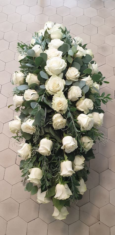Corona funebre di rose bianche con fogliame verde su un pavimento piastrellato