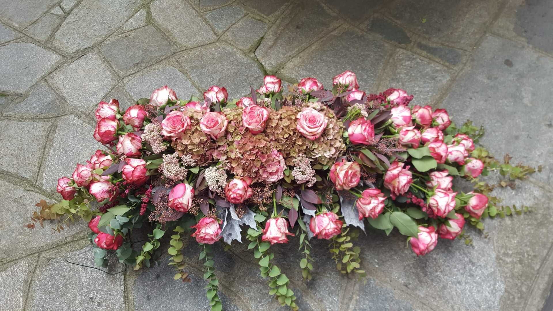 Un mazzo di rose rosa e verde adagiato su un marciapiede grigio.