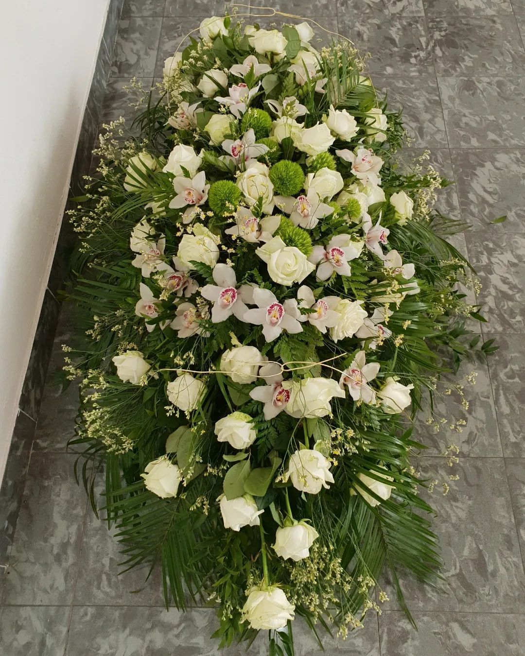 Corona funebre floreale bianca e rosa pallido con fogliame verde su sfondo grigio