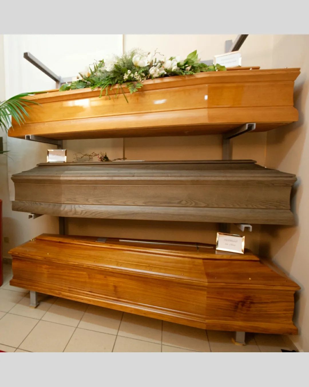 In uno showroom sono esposte tre bare aperte, con finiture in legno beige, grigio e marrone.