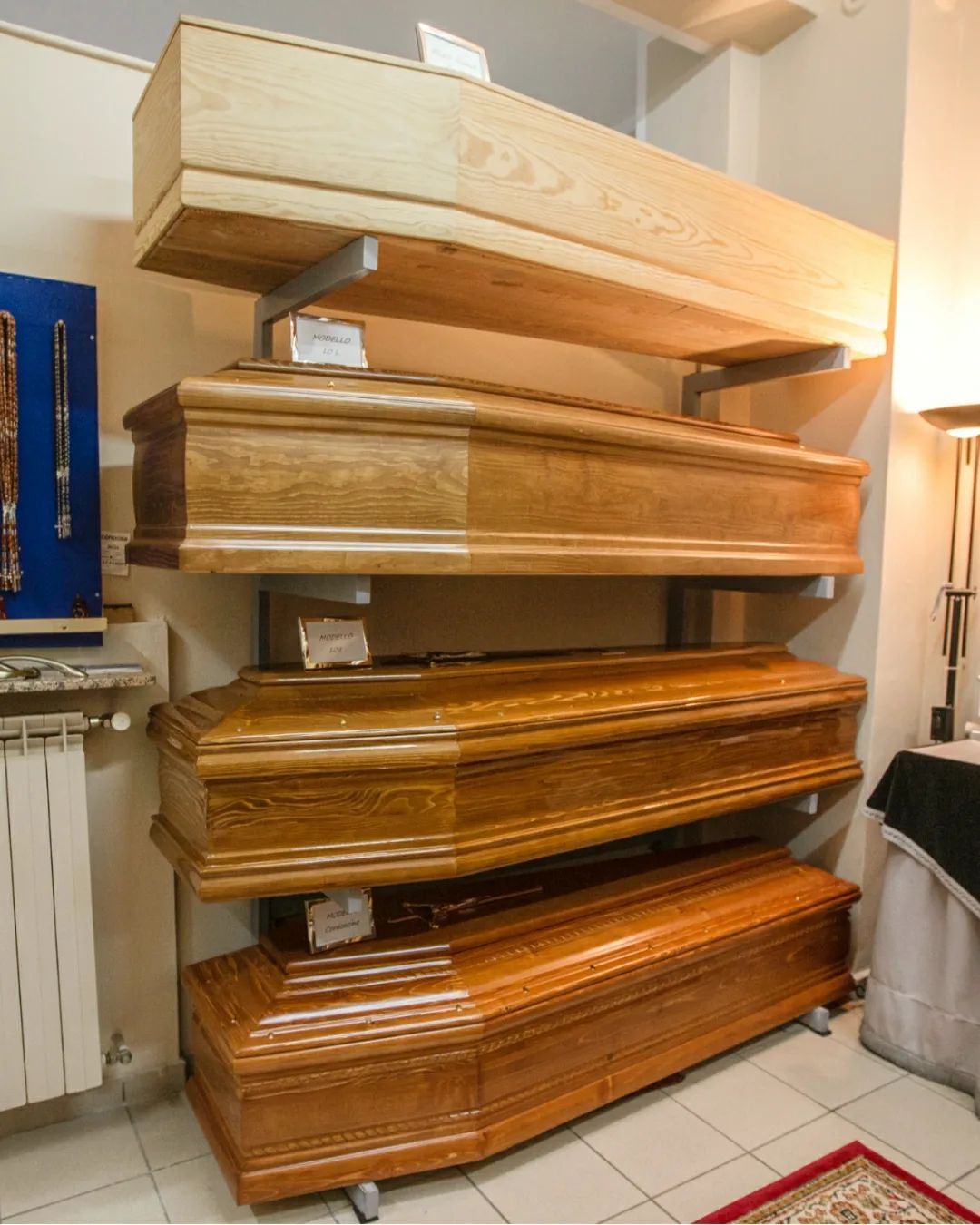 Bare di legno impilate verticalmente, con finiture chiare e scure, esposte nello showroom di un'impresa di pompe funebri.