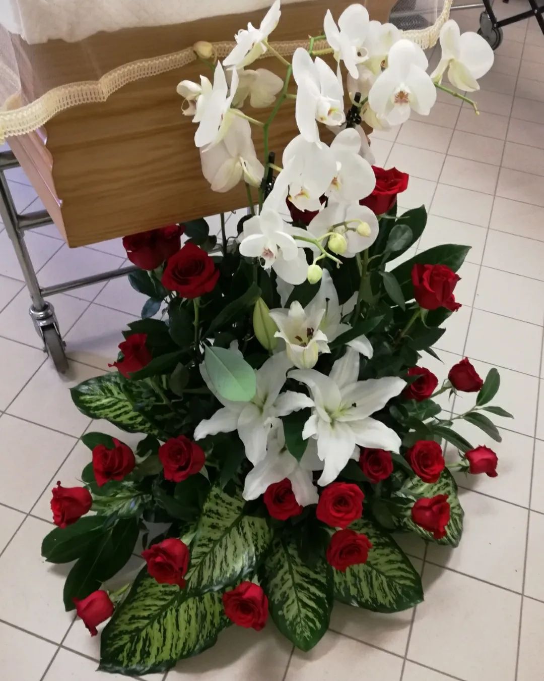 Orchidee bianche e gigli con rose rosse in una composizione floreale su un pavimento piastrellato.
