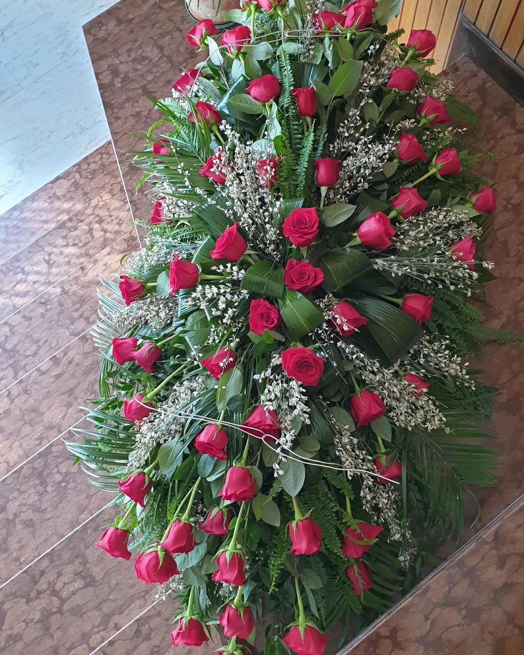 Composizione floreale con rose rosse e gypsophila bianca su un letto di verde, disposta su un pavimento piastrellato.