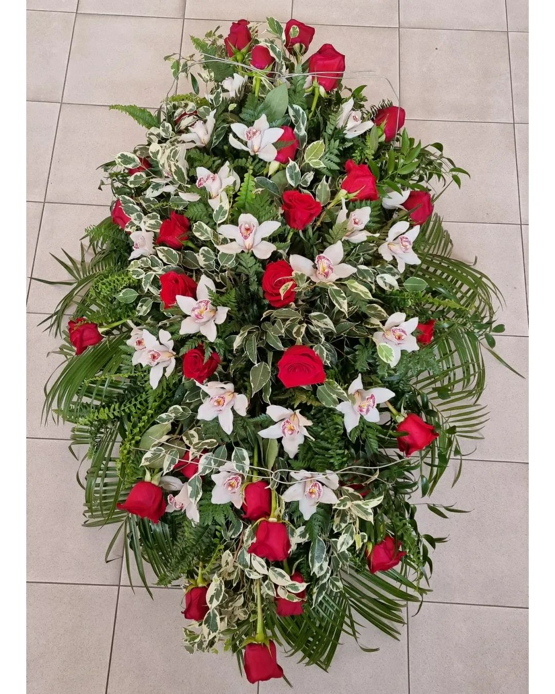 Corona funebre floreale rossa e bianca con foglie di palma verdi su un pavimento piastrellato