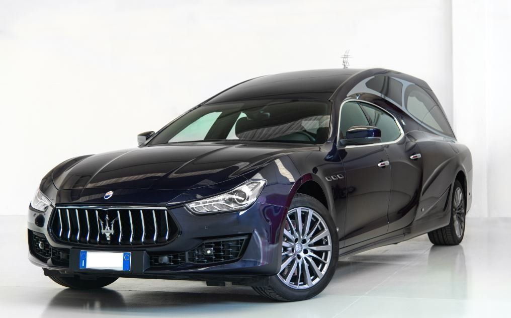 Berlina di lusso blu scuro in studio, mostrata frontalmente a sinistra su sfondo bianco.
