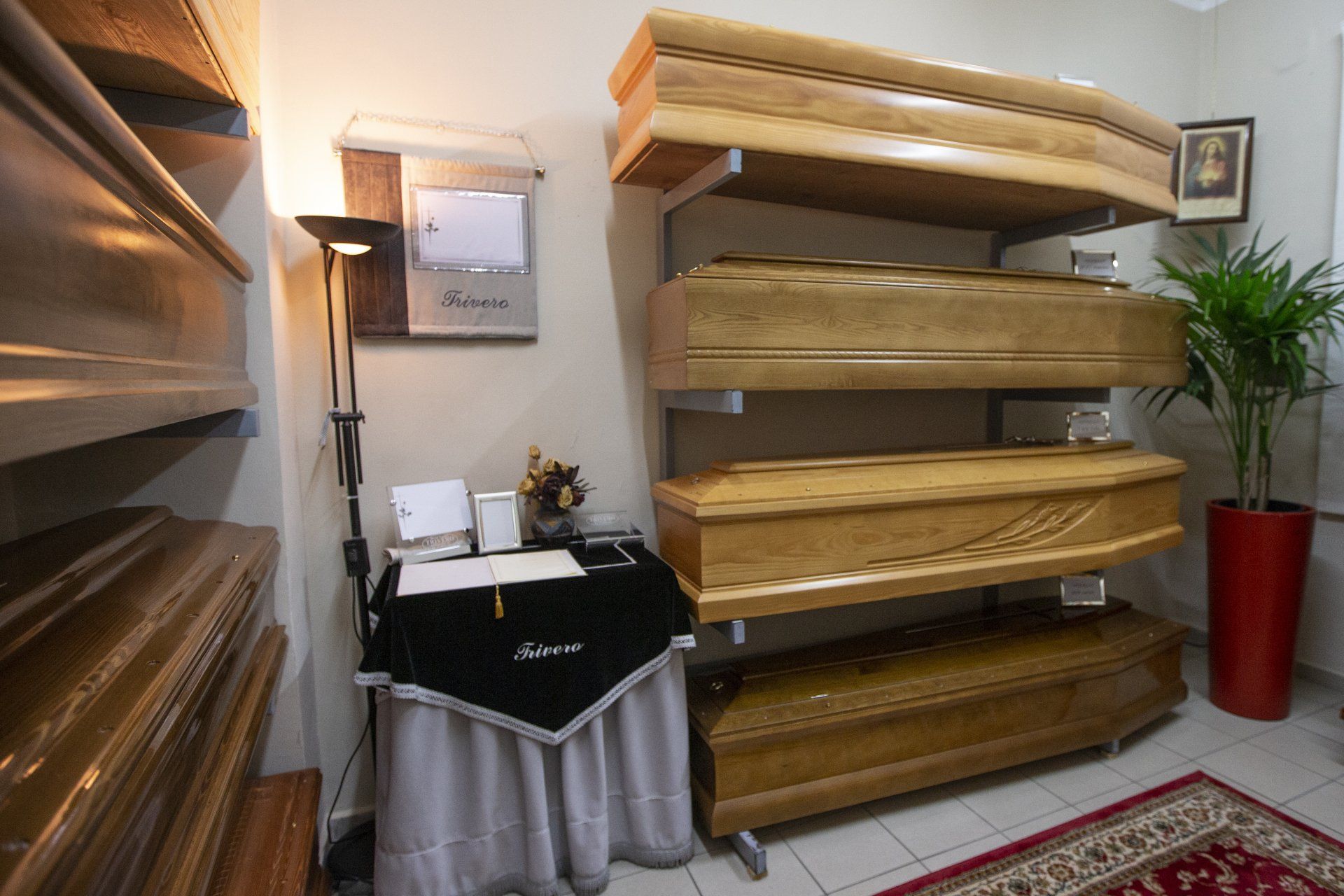 Showroom con scaffali in legno impilati a forma di bara, un tavolo nero, una lampada da terra e una pianta in vaso.