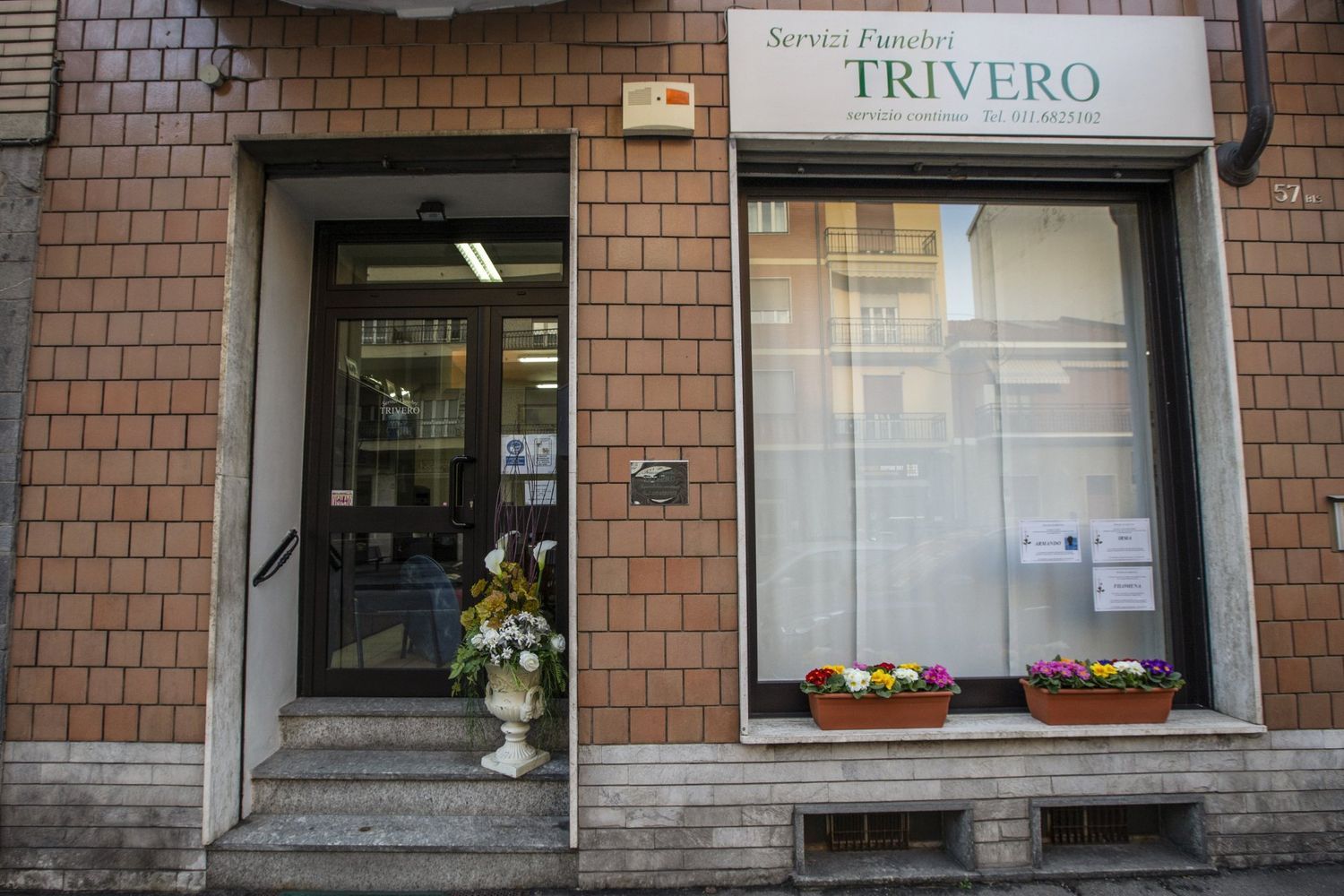 Vetrina con insegna TRIVERO, porta a vetri e fioriere sulla facciata di un edificio in mattoni.