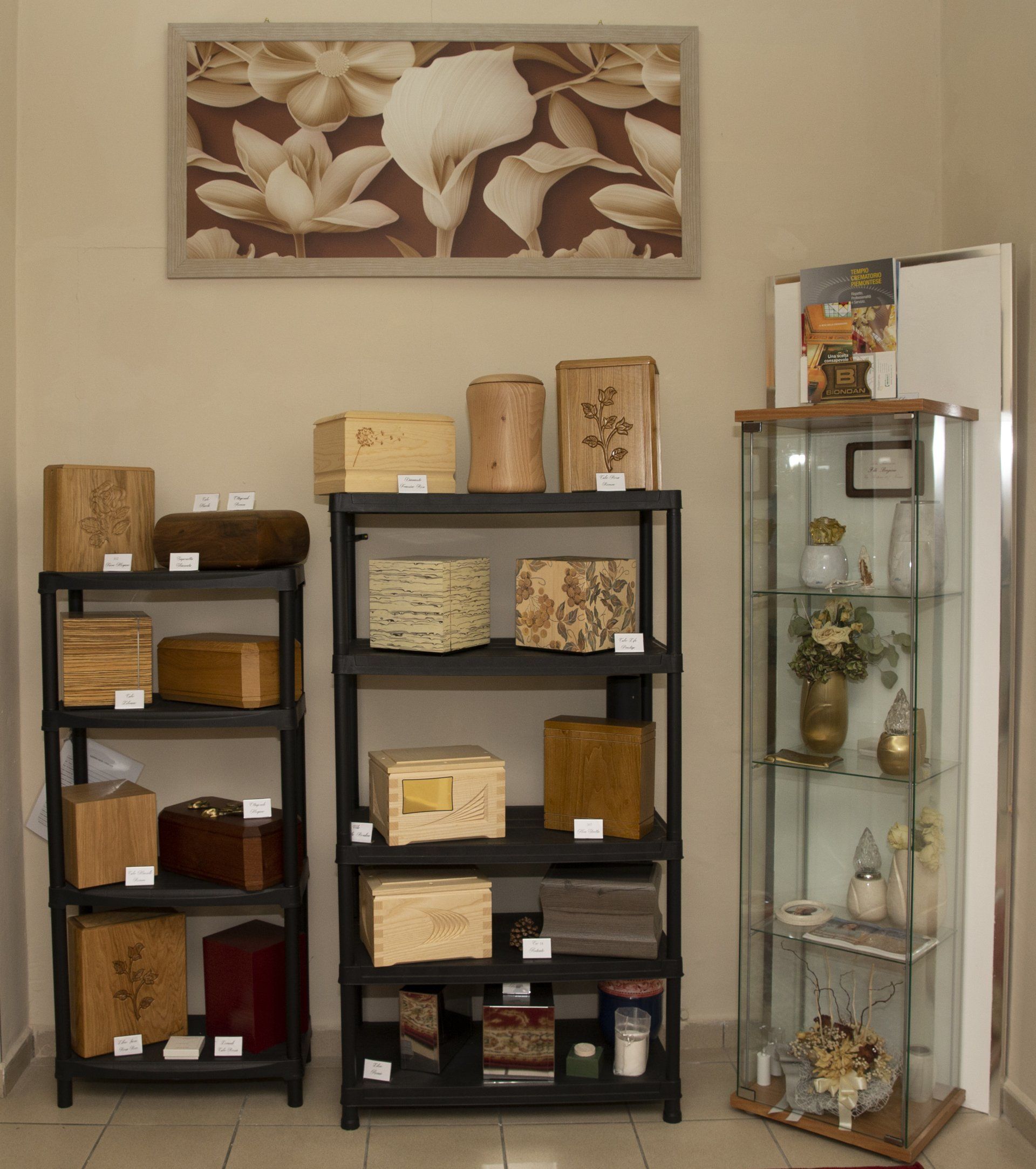 Due mensole nere e una vetrina contenente scatole decorative e ornamenti, addossate a una parete beige.