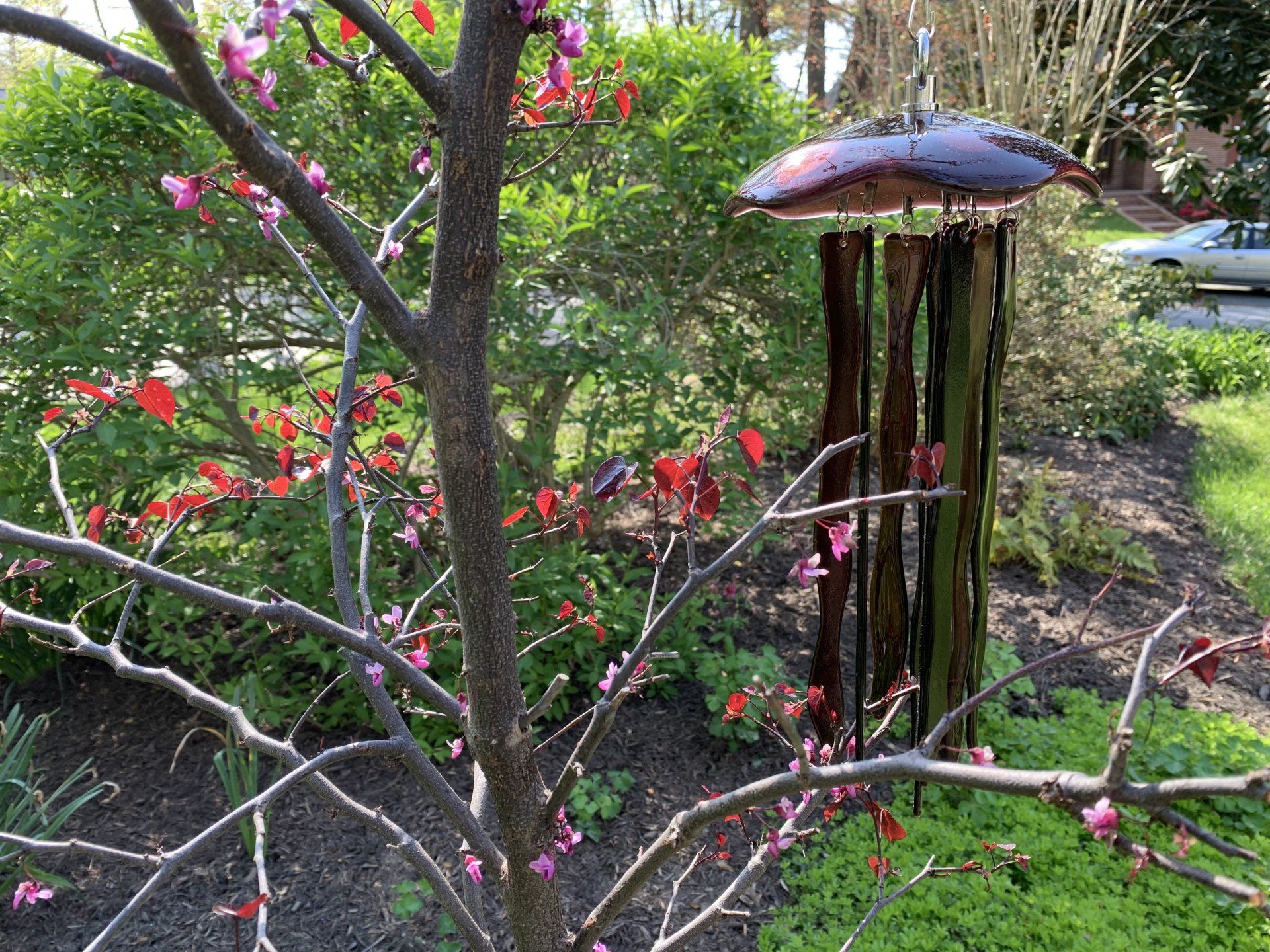 fused glass purple jellyfish wind chime hanging from a herron made of rock nd metal