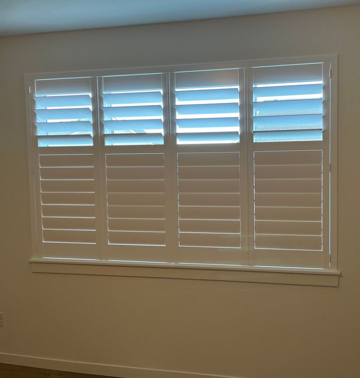 Four white plantation shutter panels covering a window, with top and bottom sections allowing for light adjustment.