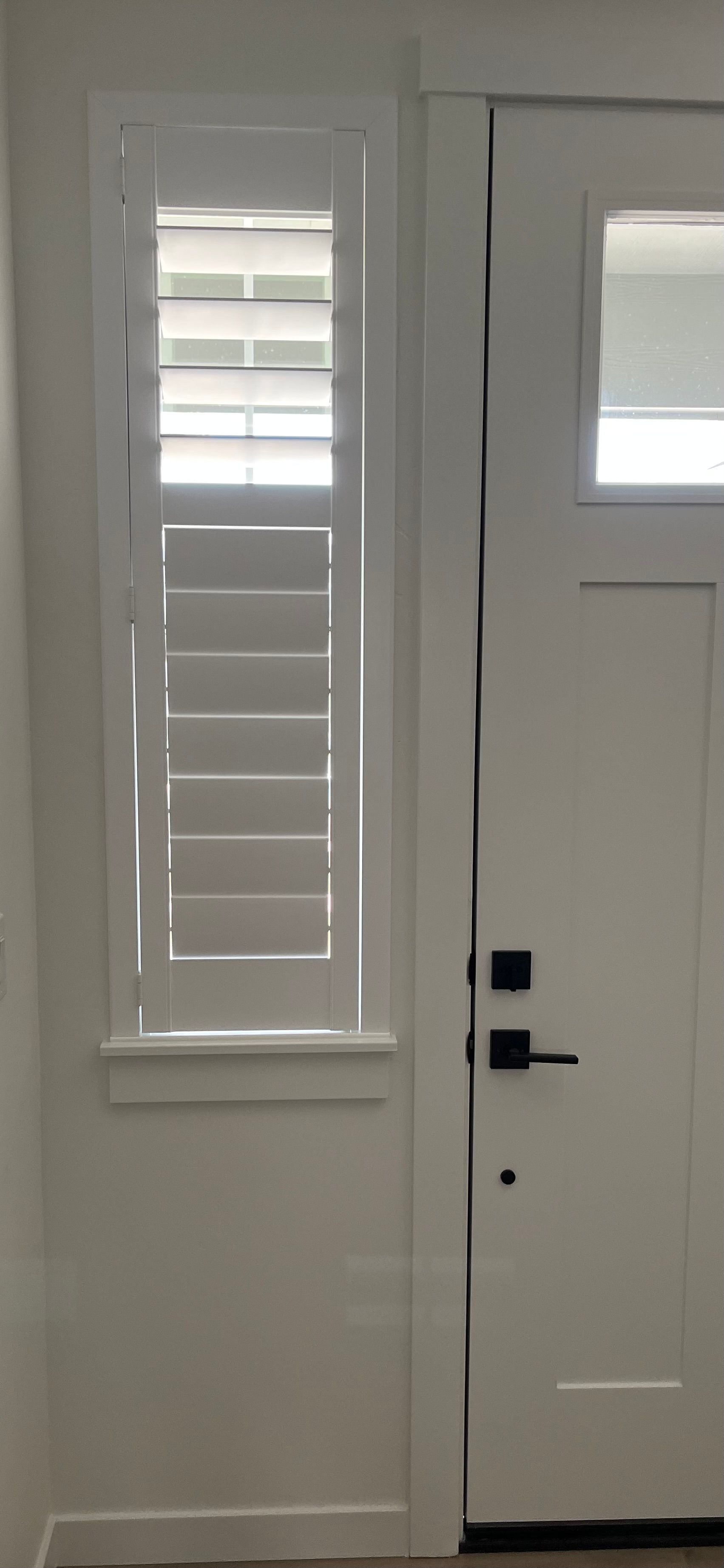 A white front door with a window sits beside a tall, narrow side window covered with white plantation shutters.