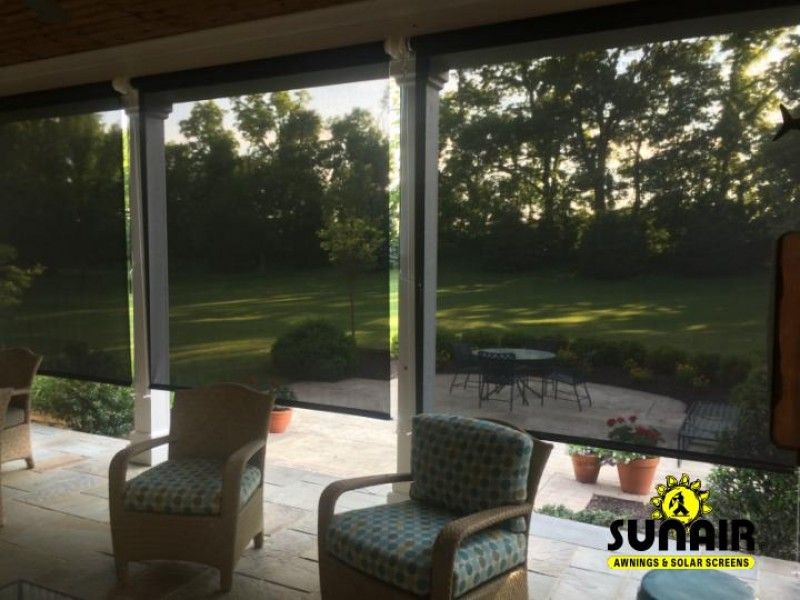 Screened porch with wicker chairs overlooking a green backyard at sunset