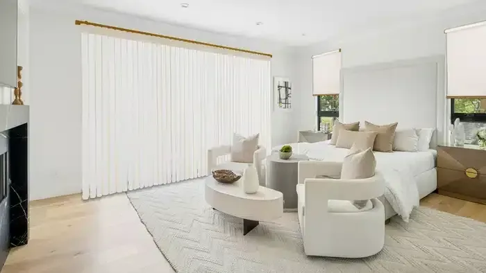 Bright modern living room with white curved sofas, beige rug, and vertical blinds over large windows