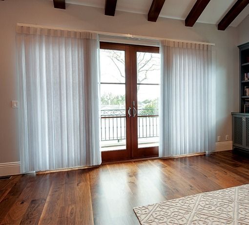 Empty living room with hardwood floors, French doors, and sheer white curtains