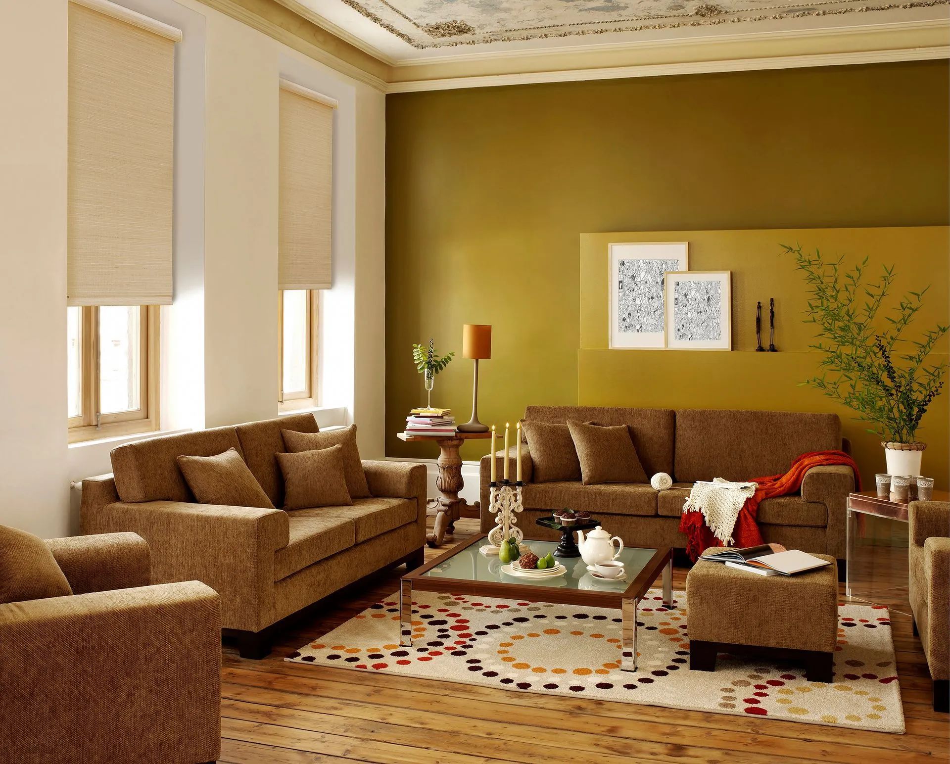 A living room features brown sofas, a glass coffee table, a patterned rug, and gold-colored walls with framed art.
