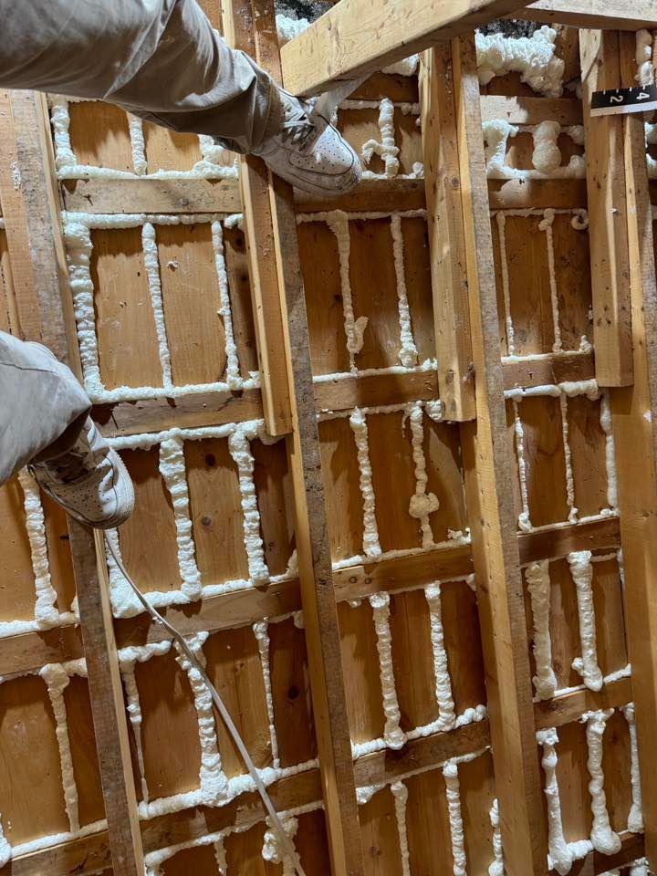 Gloved hands inspecting wooden wall framing with white insulation foam between studs