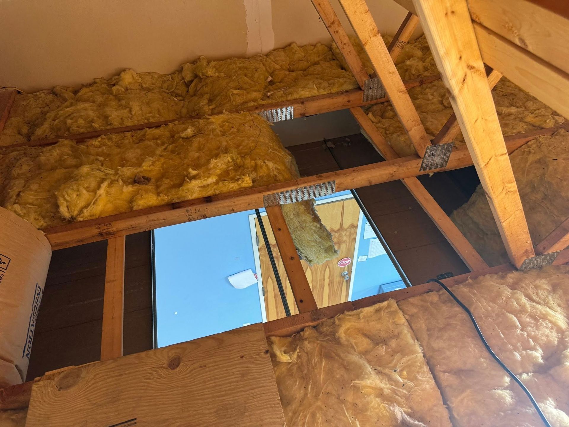 Open ceiling with exposed wood beams, insulation, and a small skylight opening to blue sky.