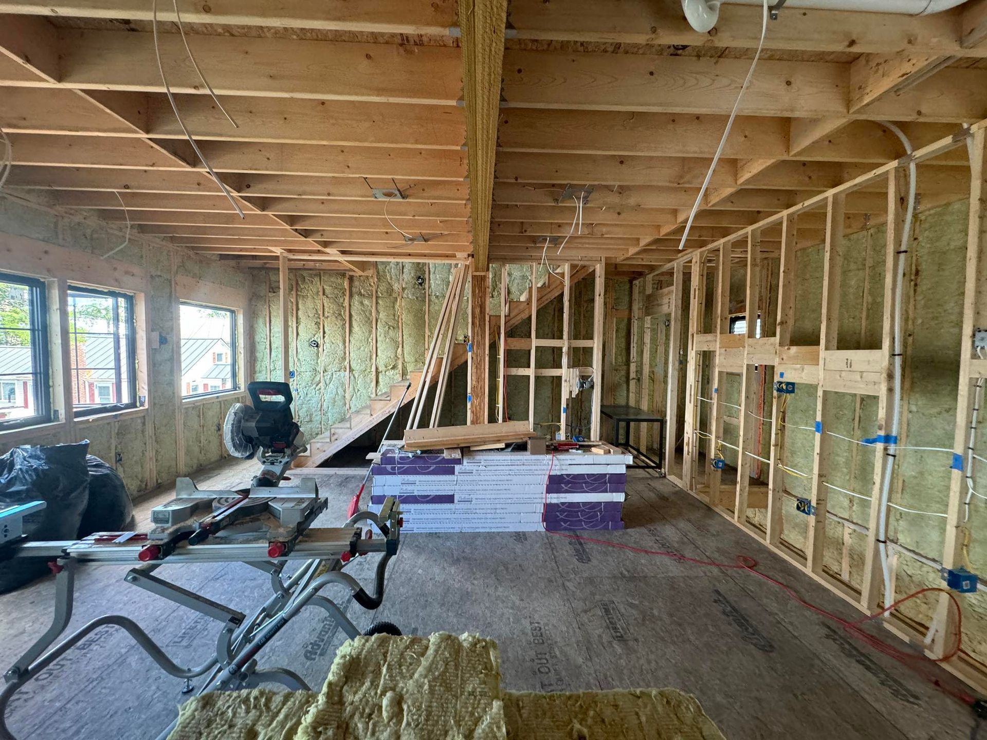 Interior of a house under construction with exposed framing, insulation, windows, and tools on the floor