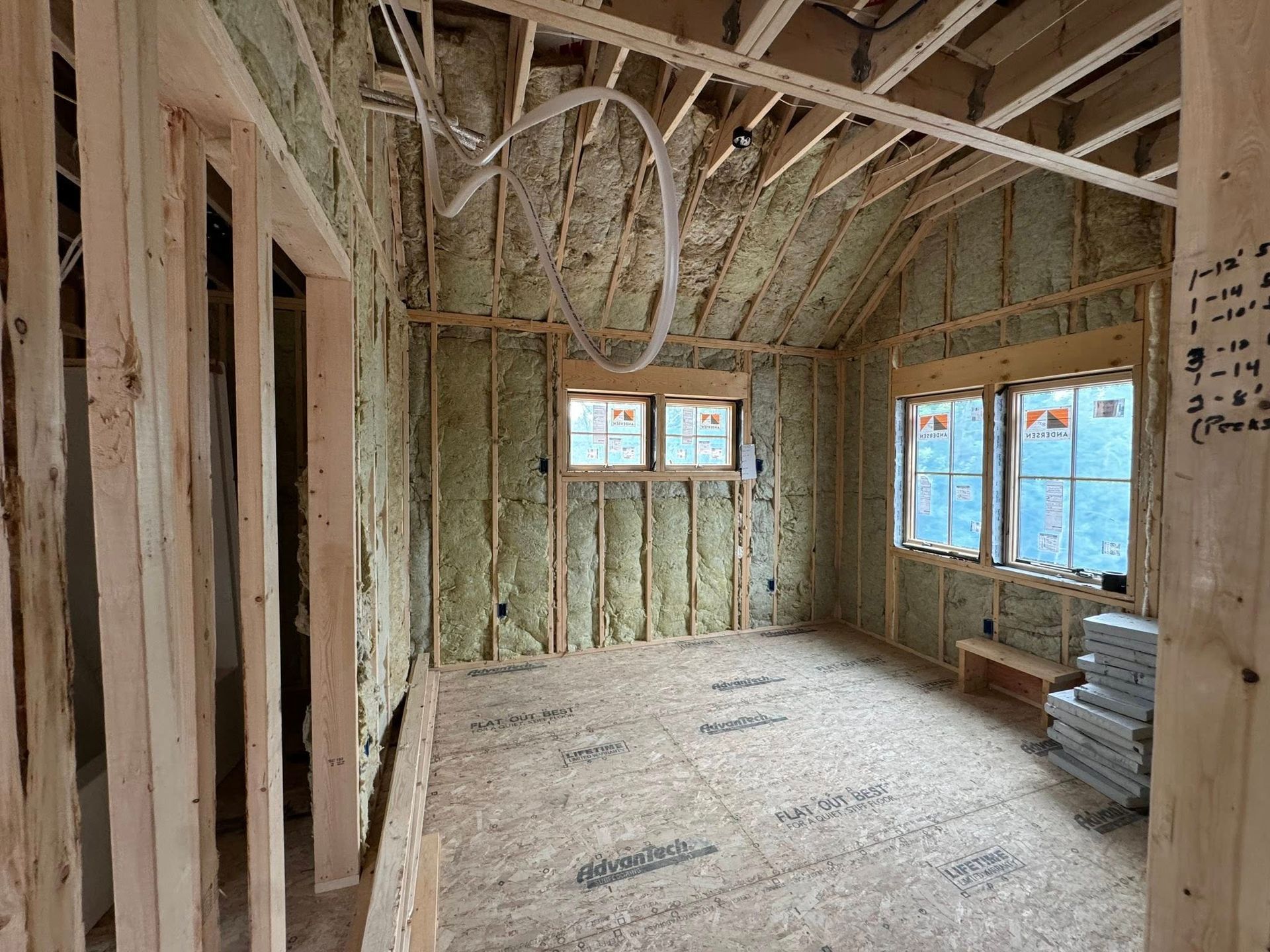 Unfinished room with exposed wood framing, insulation, and windows letting in daylight.