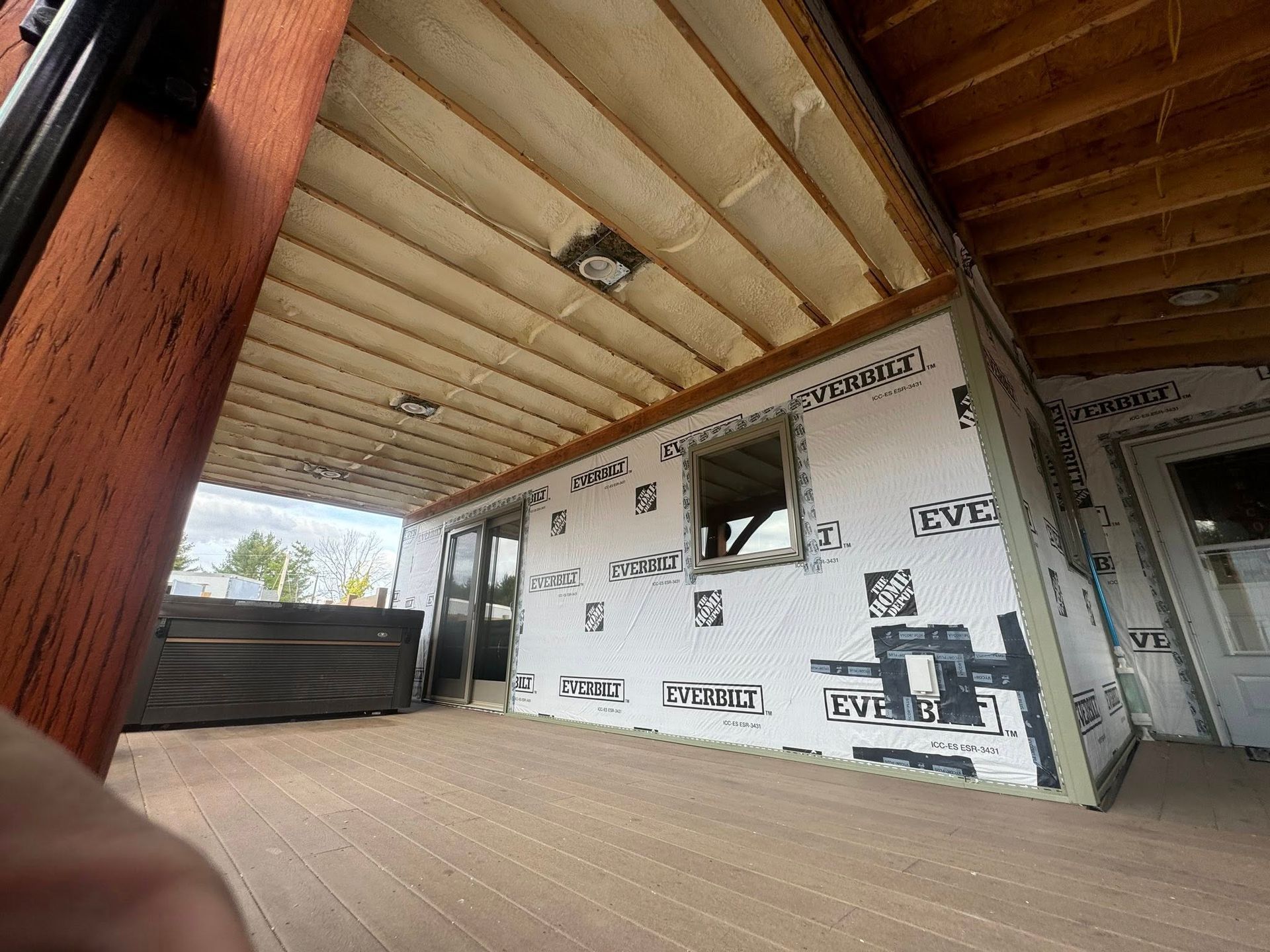 Partially built patio with exposed roof beams, white wall wrapping, and a small window opening