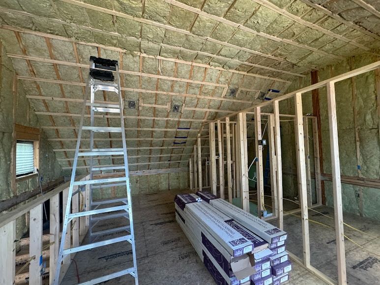 Unfinished attic with insulated sloped ceiling, ladder, exposed framing, and stacked building materials.