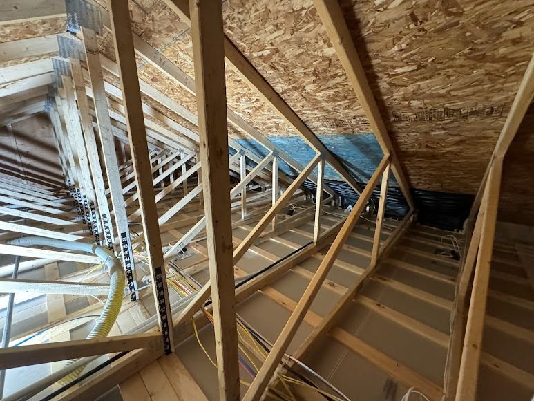 Attic interior with wooden roof trusses and exposed insulation under sloped rafters