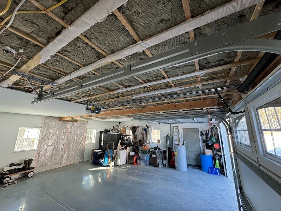 Garage interior with unfinished ceiling, concrete floor, and stored tools and supplies against the back wall