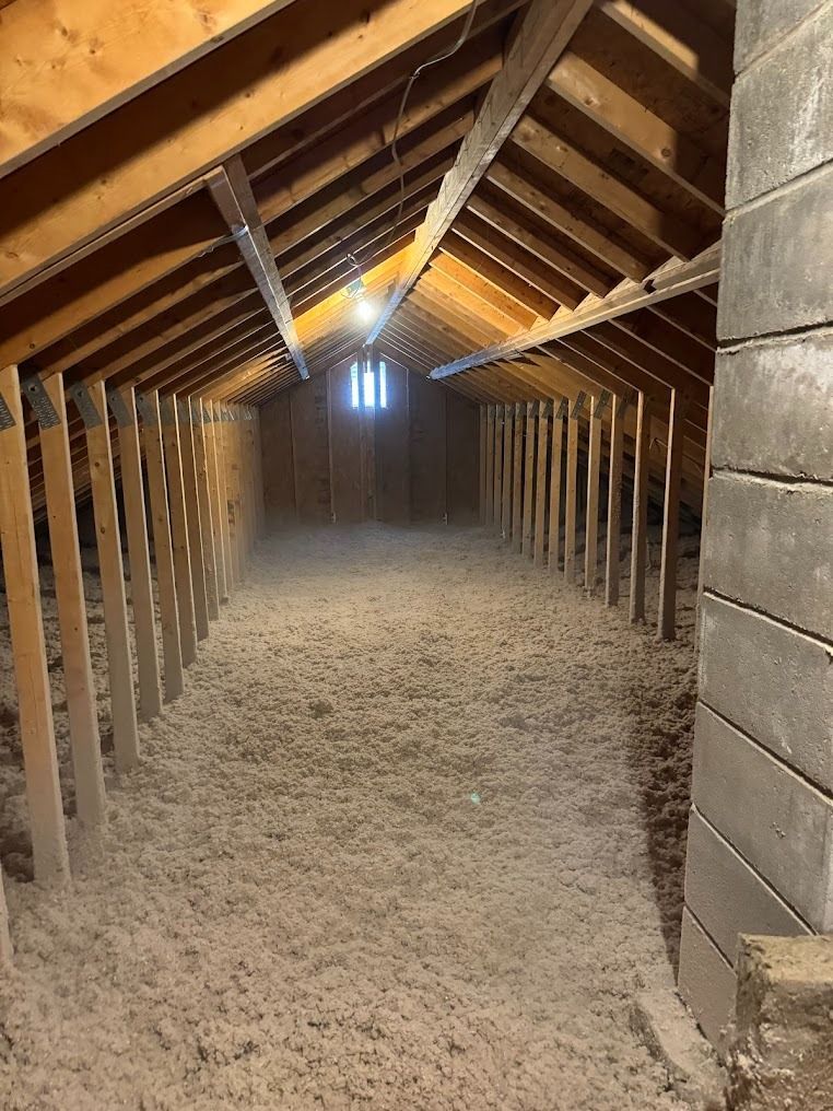 Empty attic with exposed wooden rafters, a dusty floor, and stacked cinder blocks along the right wall.