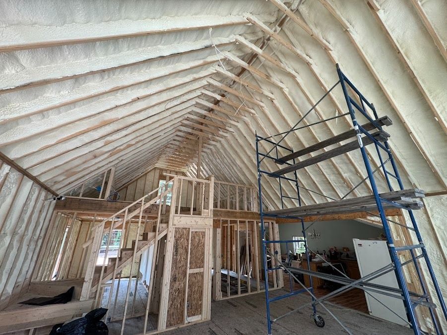 Unfinished attic interior with white spray insulation, exposed framing, and blue scaffolding.