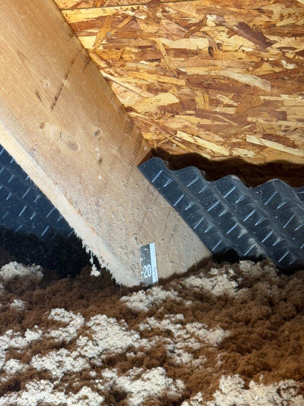 Attic insulation around a wooden beam and roof framing, with foam board and wood sheathing visible.