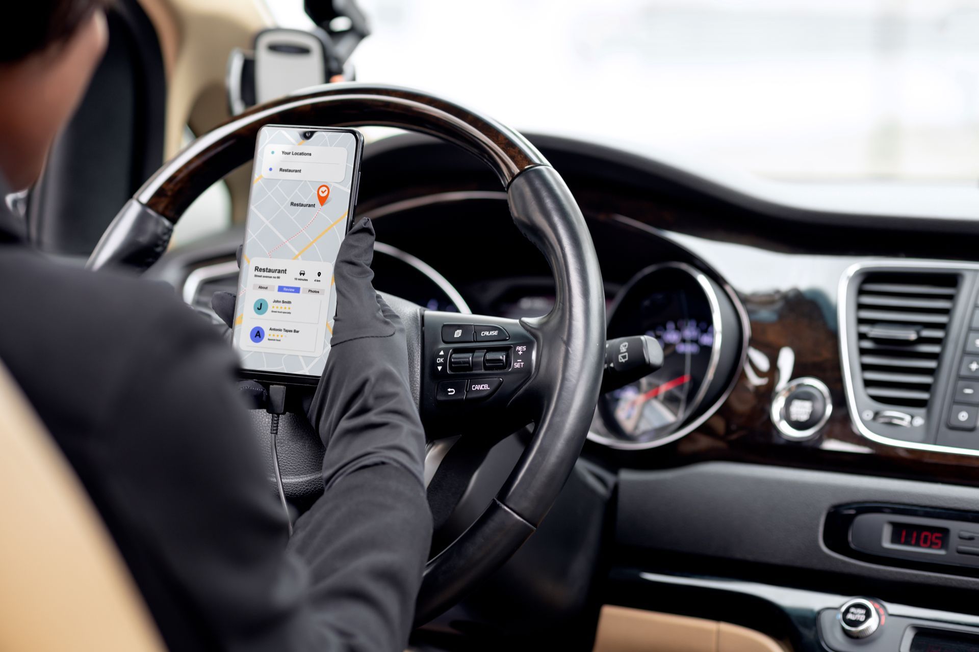 Driver in black gloves using a phone with a map app while driving in a car.