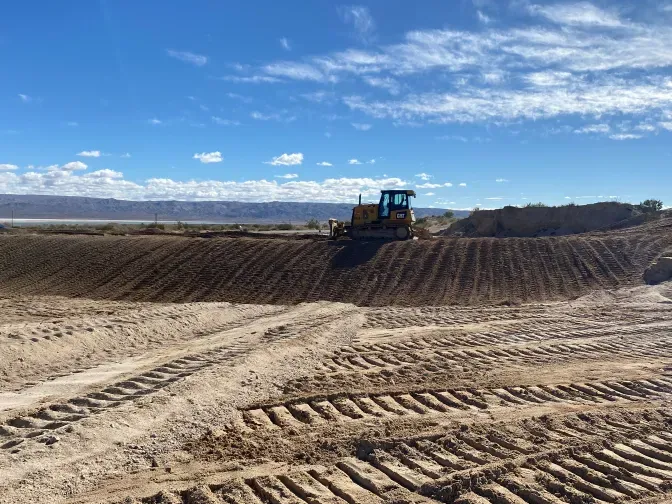 A bulldozer grading dirt on a construction site under a blue sky.