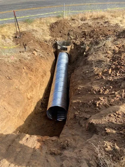 Corrugated metal pipe in a trench, next to a road.