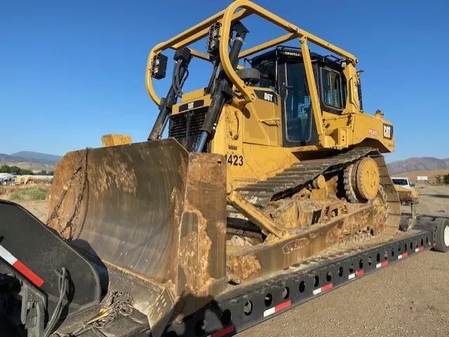 Yellow Caterpillar bulldozer on a flatbed trailer, under a clear sky.