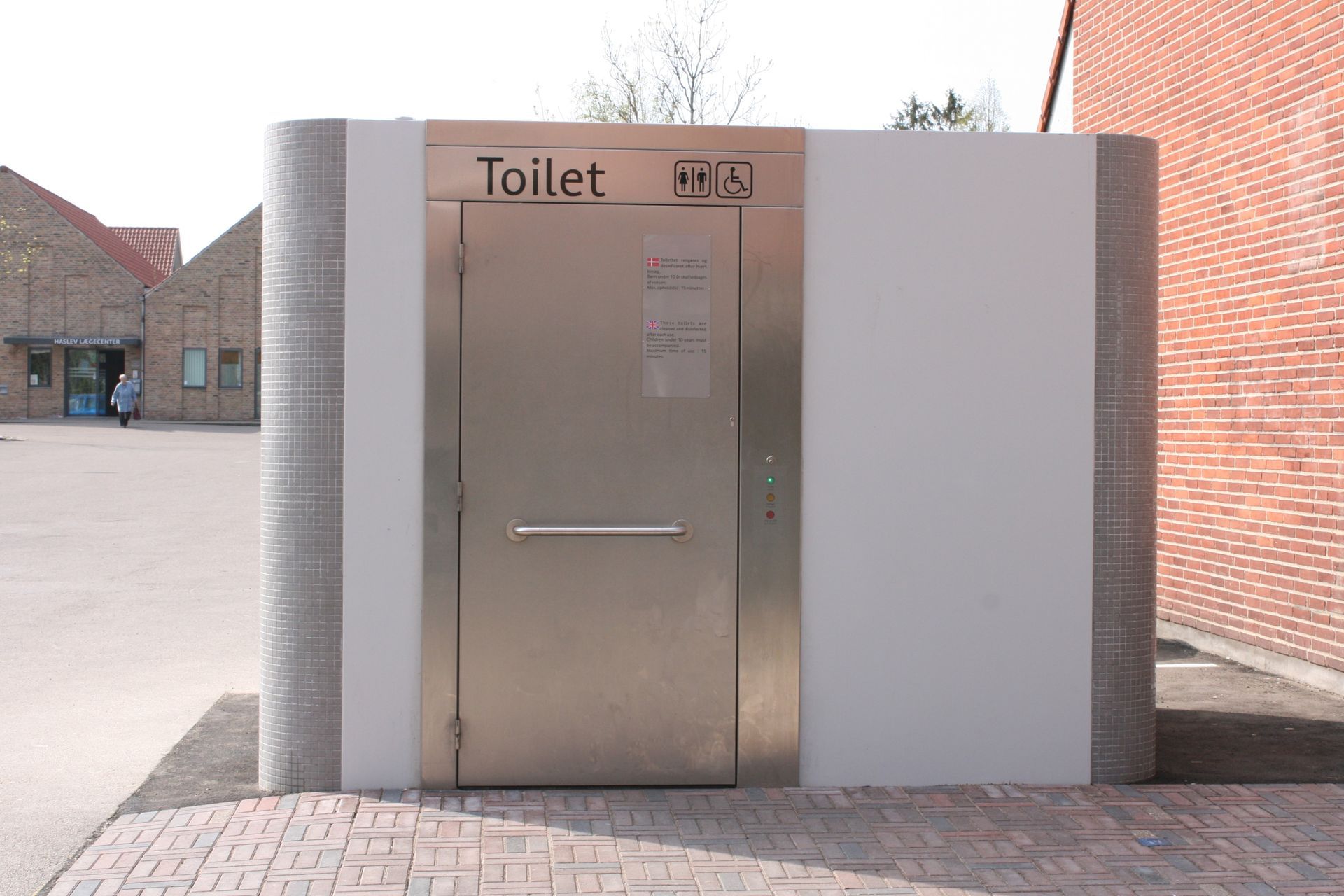 Et rustfrit stål toilet med en murstensbygning i baggrunden