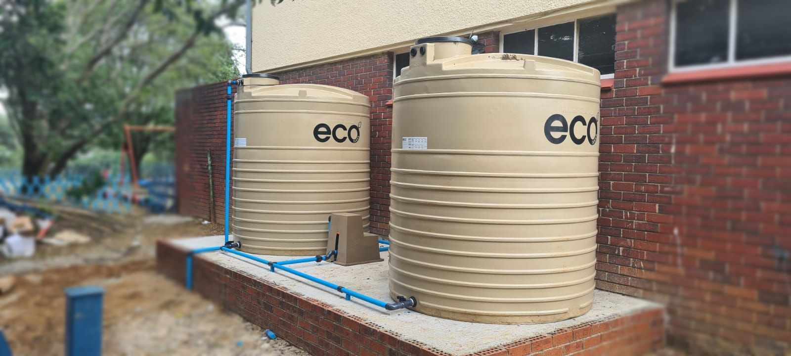 Two large water tanks are sitting outside of a brick building.