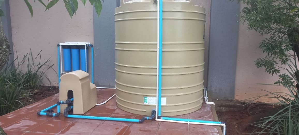 A large water tank and water filter is sitting on a sidewalk next to a building.