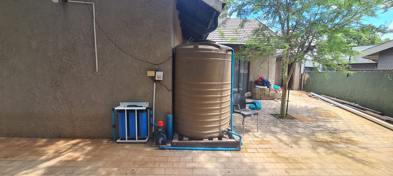 A large tan water tank with blue pipes attached to it leading to water filer