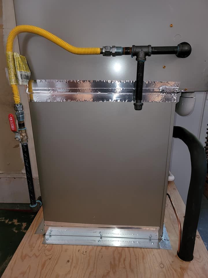 Gas furnace with yellow gas line, black pipe fittings, and vent hose on a wooden base.