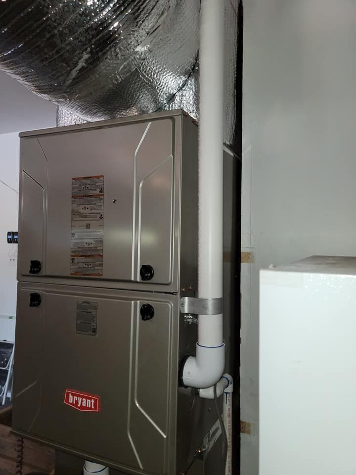A Bryant furnace unit with white PVC vent pipe in a utility room, silver ductwork above.