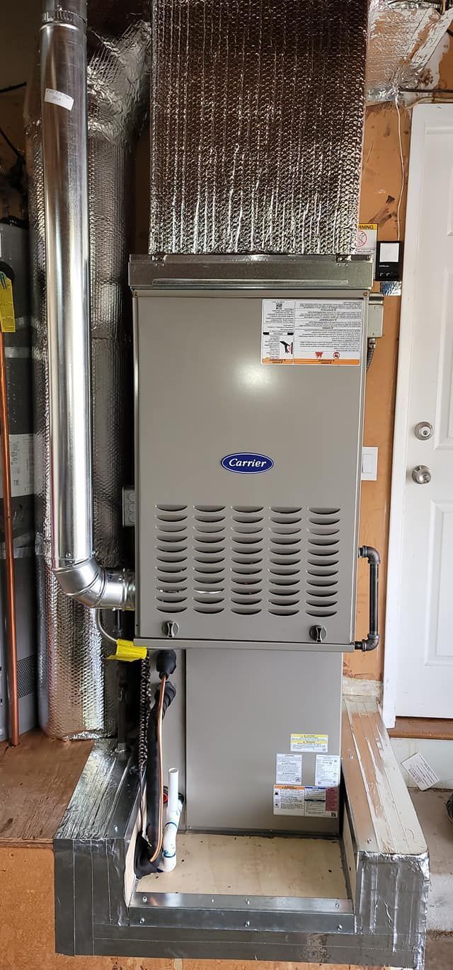 A Carrier furnace installed in a home, with silver ductwork, vents, and insulation around it.