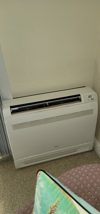 A white air conditioning unit is positioned in a corner against a beige wall.