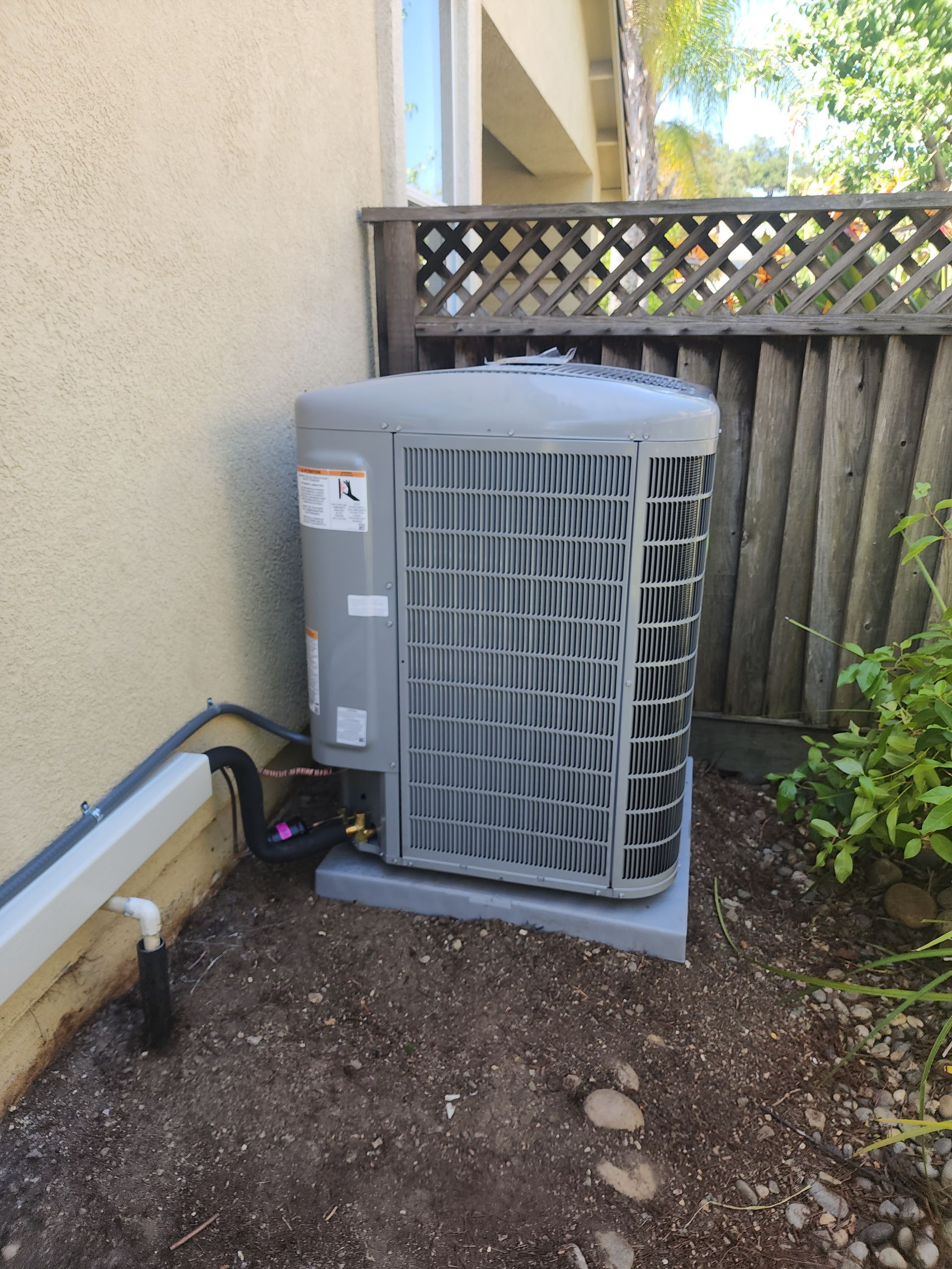 Air conditioning unit on a concrete pad near a wall and wooden fence.